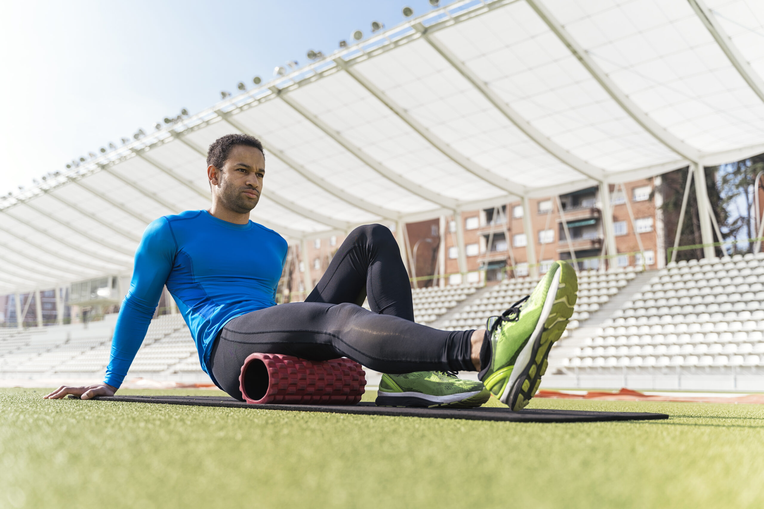 male athlete sitting on the track stretching his legs with foam roller.