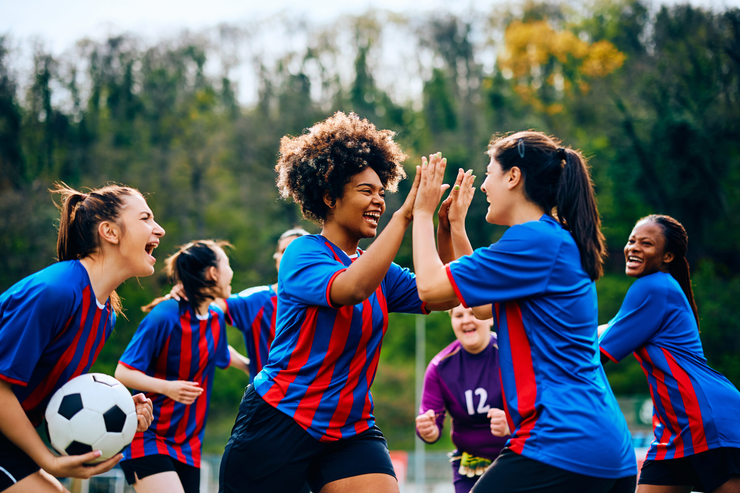 Cheerful female players congratulating each other after scoring a goal during soccer match on playing field.