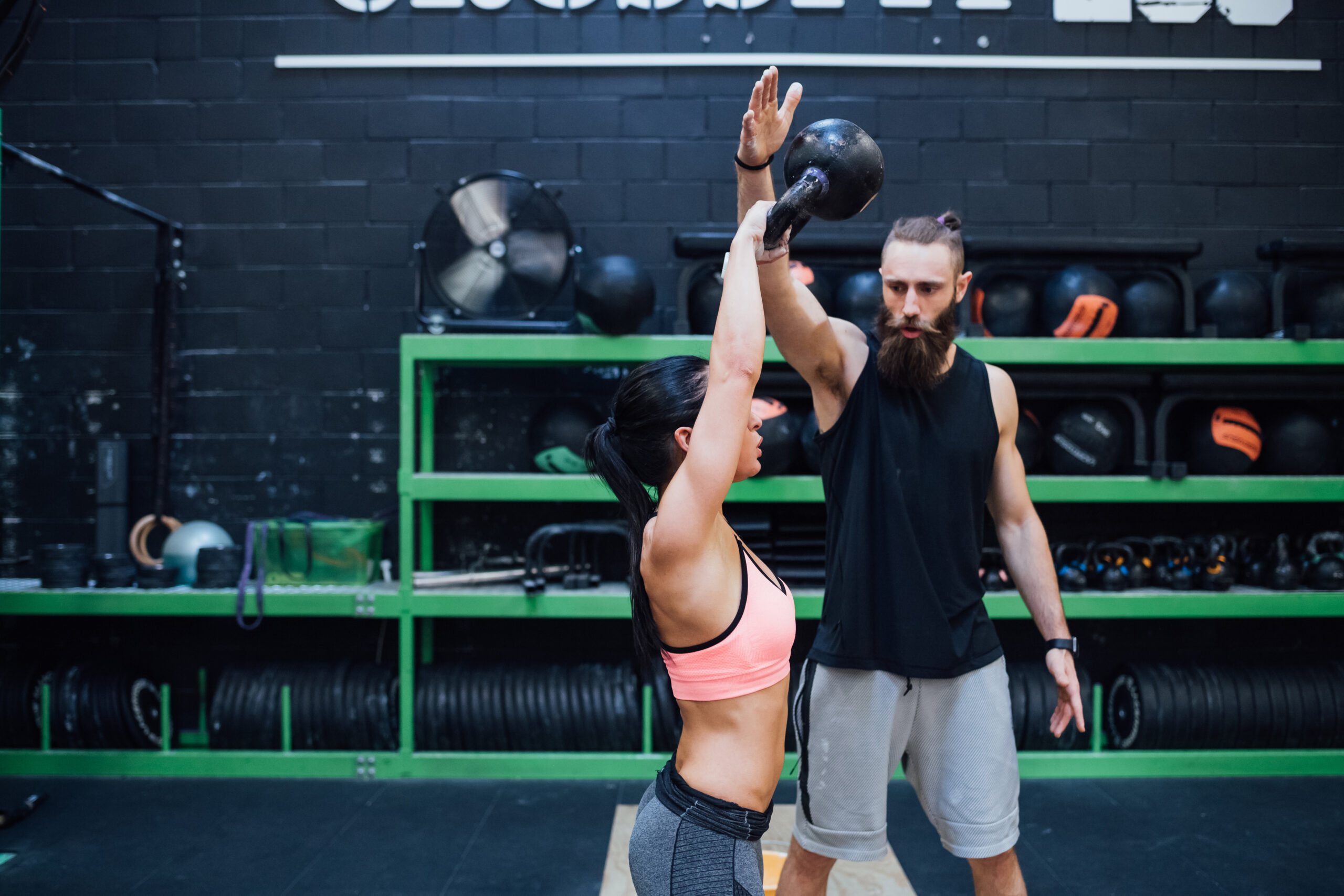 Young woman training with kettlebell helped by her personal trainer - woman power, fitness, cross fit concept